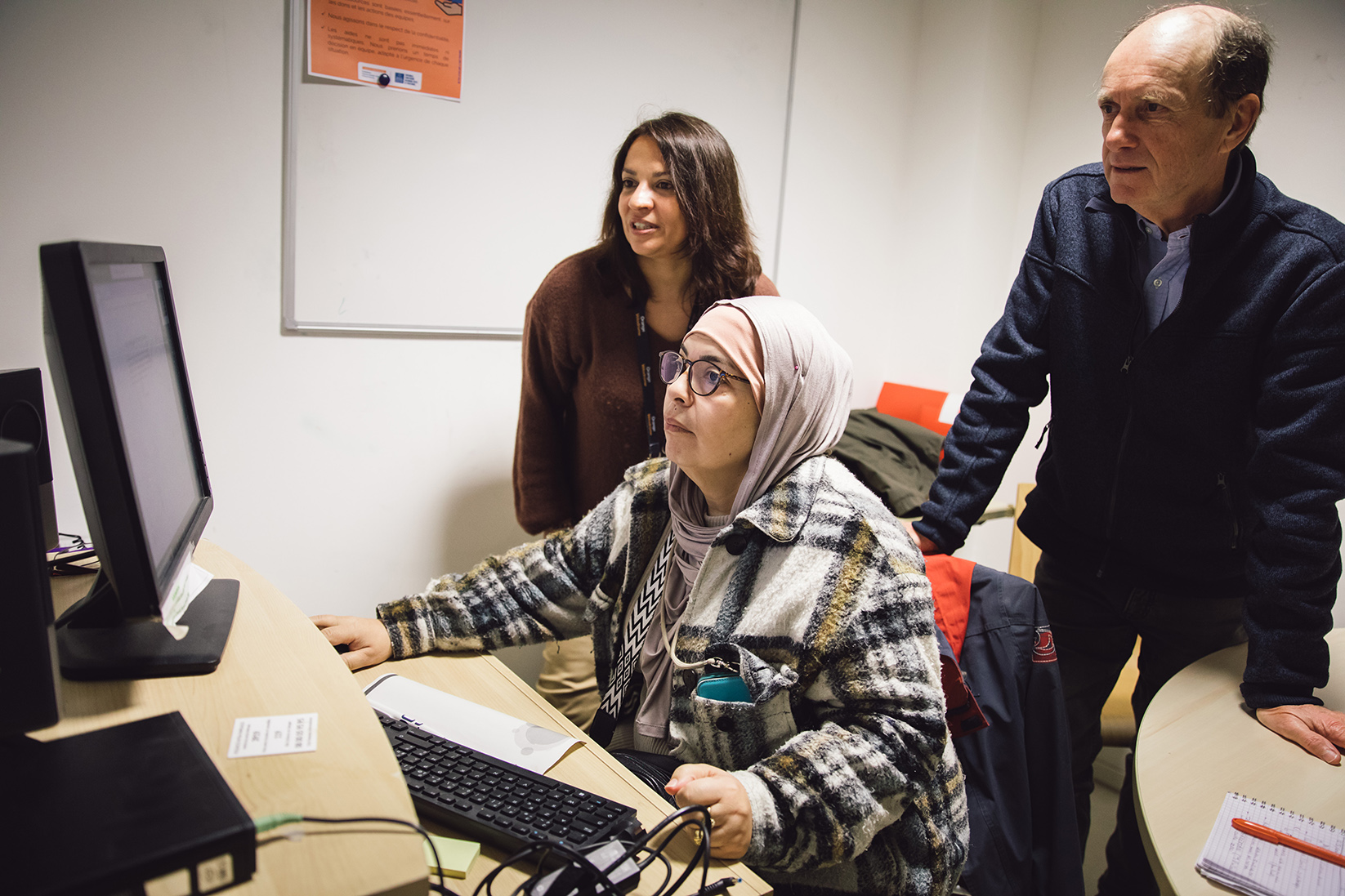 Halima devant l'ordinateur et deux bénévoles de l'atelier numérique
