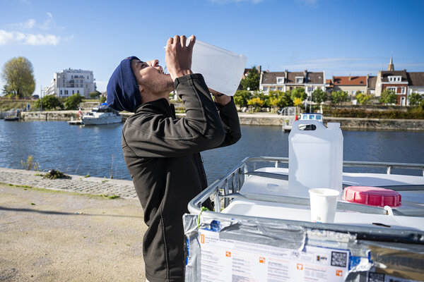 Un jeune homme boit de l'eau à un bidon.