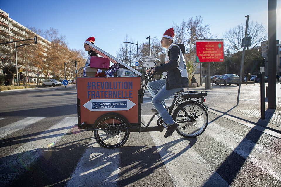 un tripoteur aux couleurs du Secours Catholique traversant une rue