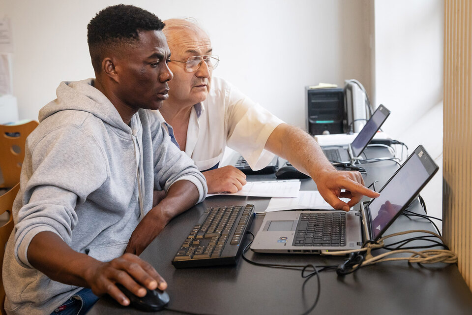 Un bénévole accompagne un jeune homme dans l'utilisation d'un ordinateur